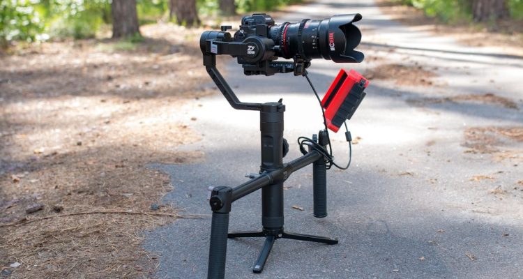 A professional camera on a gimbal setup in a peaceful forest pathway.
