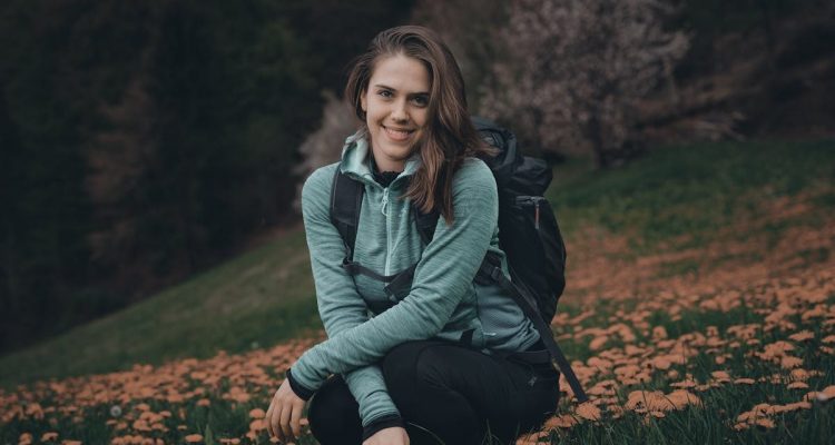 Teen girl with backpack enjoys scenic meadow in Slovenia, surrounded by blooming wildflowers.